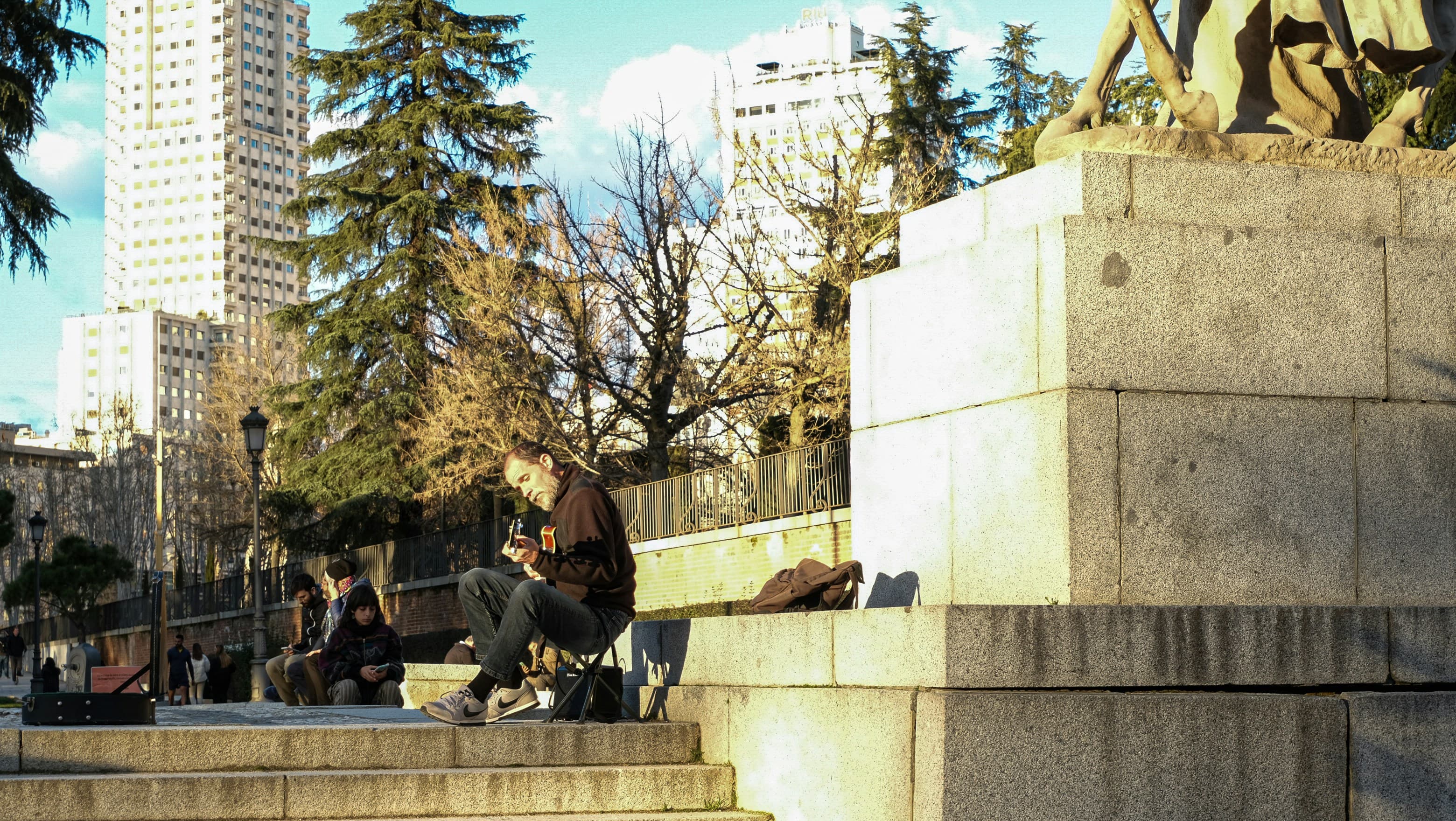People sitting on stone steps below a monument in winter sun