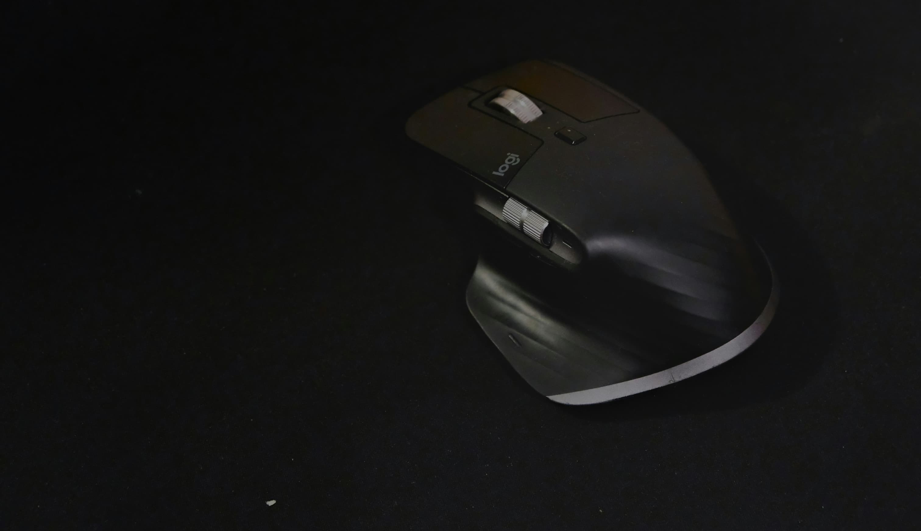 An MX Master 3S on a black mat, seen from above, with the thumb wheel on its near side