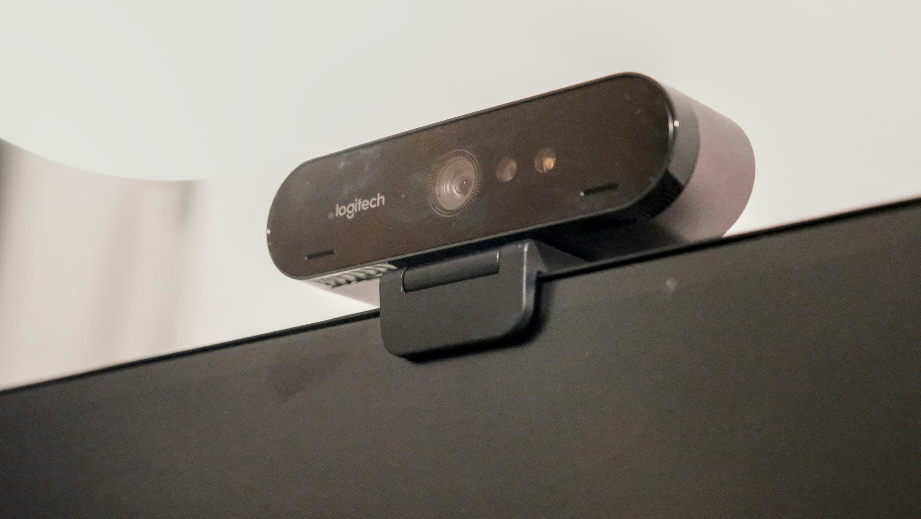 A webcam clipped to the top edge of a monitor, seen from below against a white wall