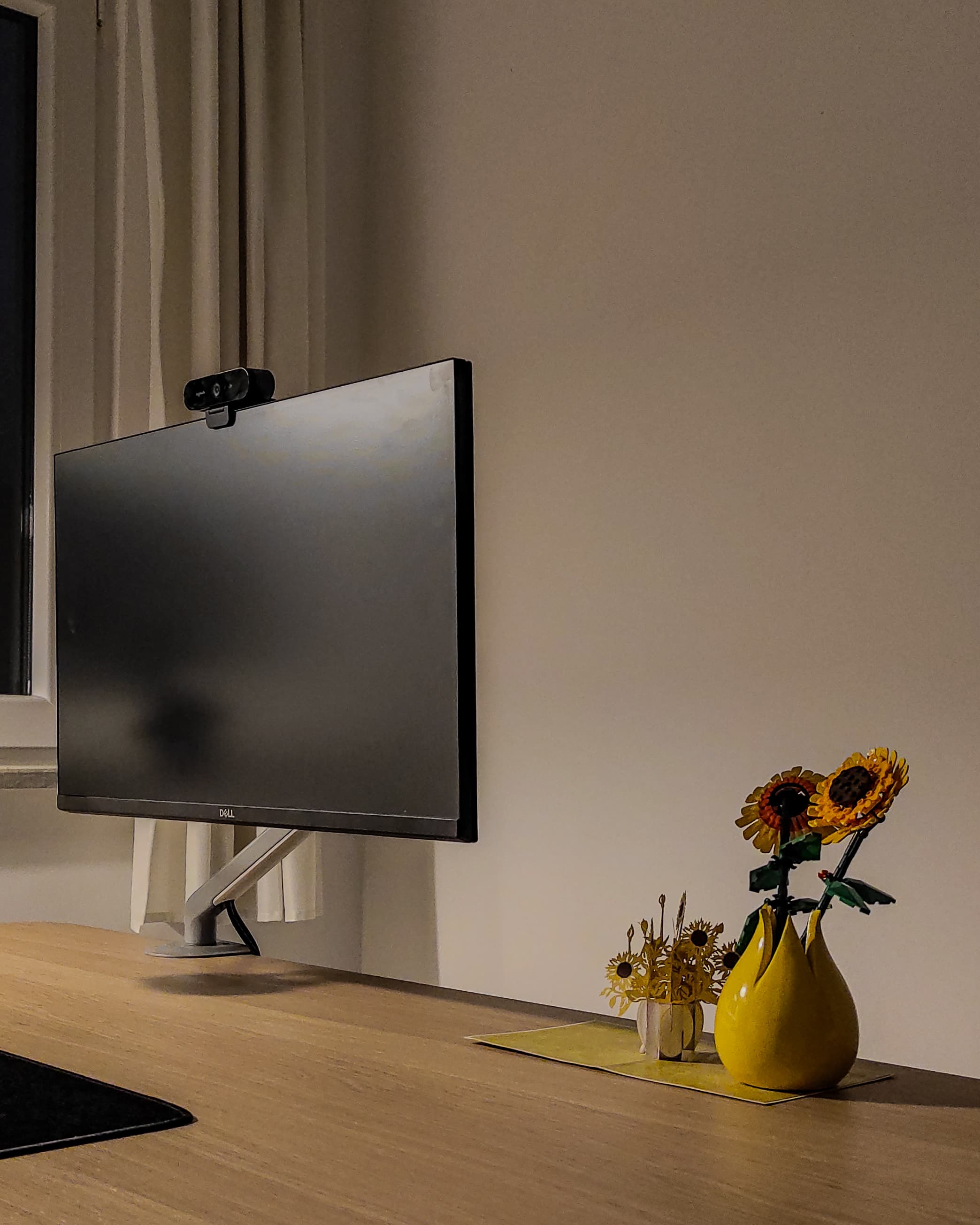 The Dell held out over the desk on a white arm, a webcam clipped to its top edge